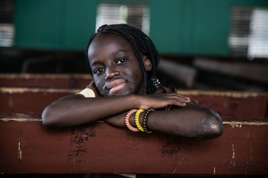 A close up photo of Rihanata posing on a church pew. The background is dark green.